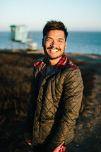 smiling man in a coat standing on a shore 