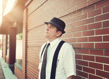 a man in a hat and suspenders looking up 