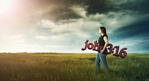 Woman carrying a sign of John 3:16 in a field
