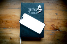 Phone with Bible on a wooden table. Blank screen for copy space.