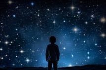 Silhouette of a young child standing and observing the night sky full of stars