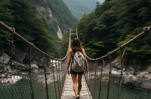 female hiker in shorts crossing a suspension bridge in a mountainous region