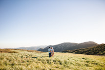 a couple walking holding each other on a mountaintop at sunset 