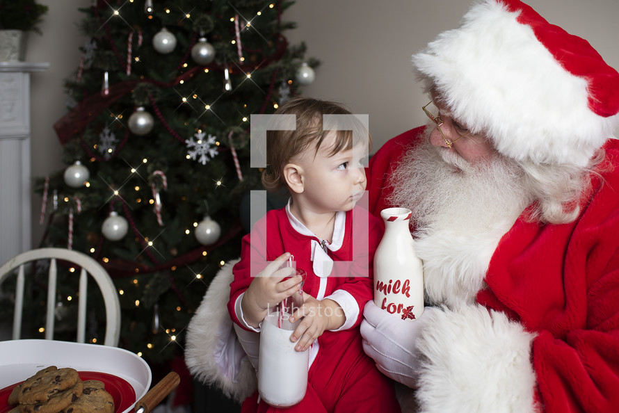 a toddler with cookies and milk sitting on Santa's lap 
