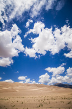 clouds in a blue sky over sand dunes 