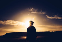 a boy standing on a beach with a sunburst 