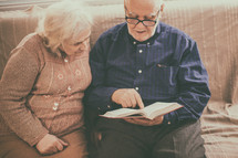 elderly couple praying and reading a Bible together 