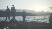 Three men walk out on rocks to the ocean with mountains in background at twilight.