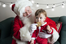 a toddler eating a cookie on Santa's lap 