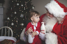 a toddler with cookies and milk on Santa's lap