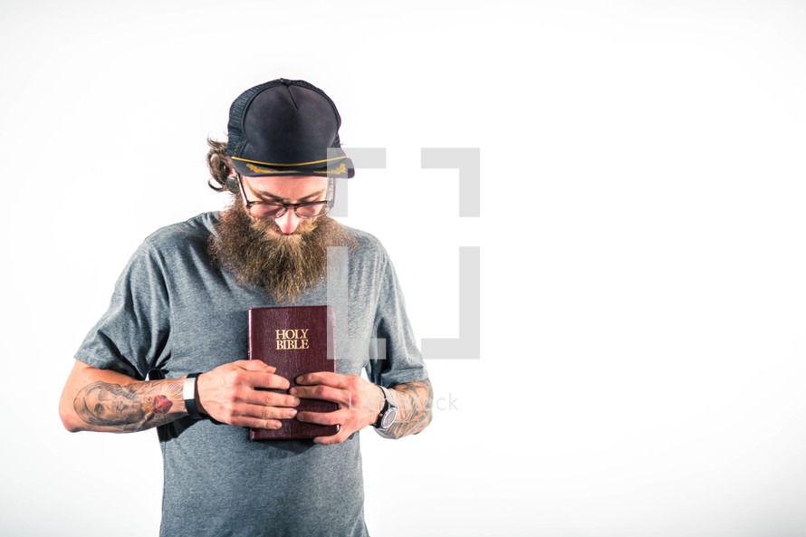 man with tattoos holding a Bible to his heart 