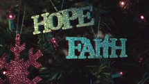 Hanging "hope" ornament on Christmas tree next to "faith" ornament