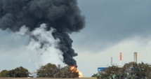 Accident in oil refinery - huge explosions and fireballs rising and thick black smoke covers the sky.