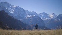 A young man walking towards camera in a mountain field with epic mountains in background