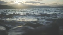 Close up of waves and ocean at sunset with mountains in background.