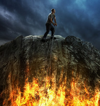 man in chains on a cliff above the flames of hell 