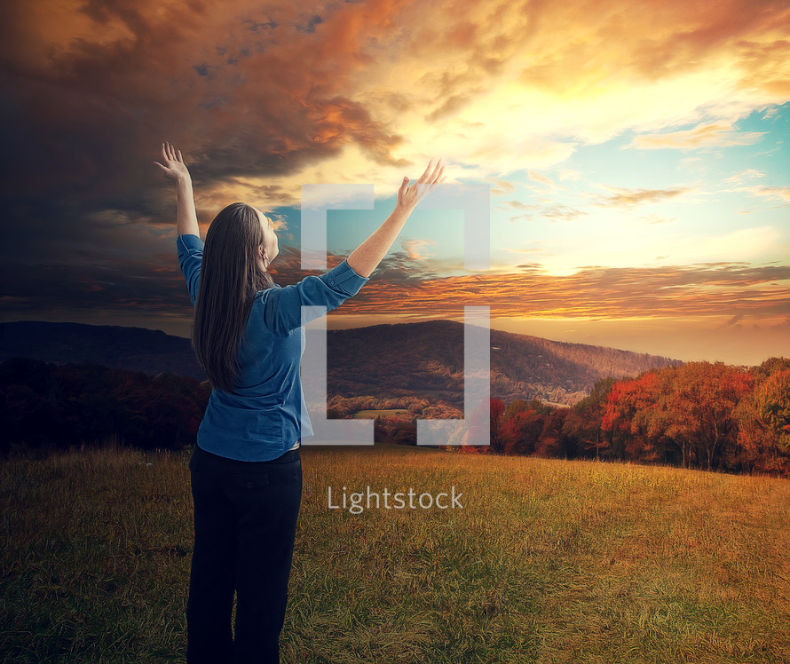 woman standing outdoors with hands raised to God 