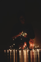 sitting holding a string of lights