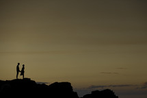 an expecting couple standing at an edge of a cliff at dusk 