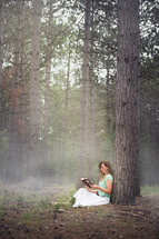 a woman sitting under a tree in a forest reading 