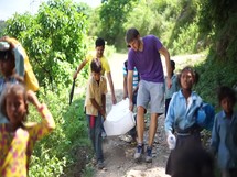 school children carrying supplies down a dirt road in Nepal 