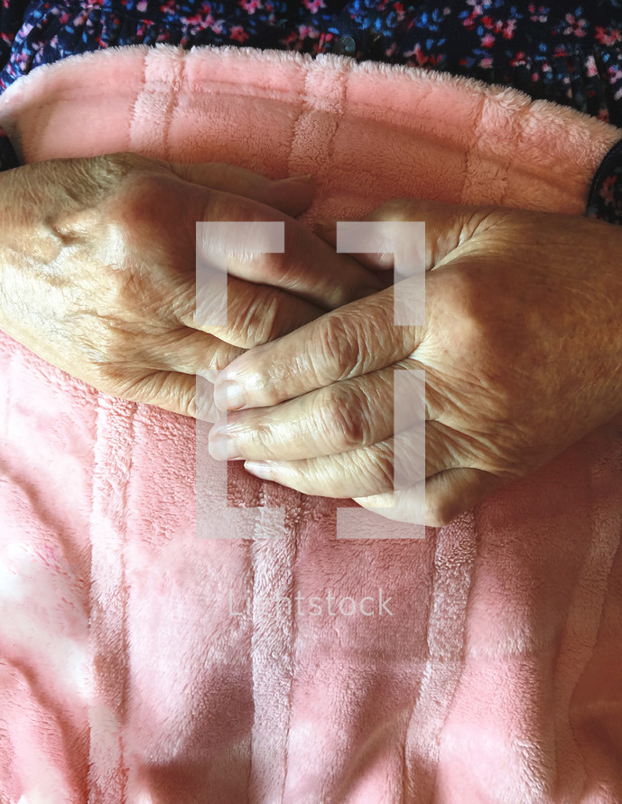 elderly hands on a pink blanket 