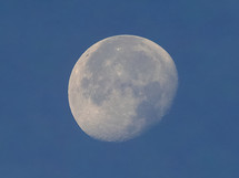 Full moon seen with astronomic telescope over blue sky in the morning