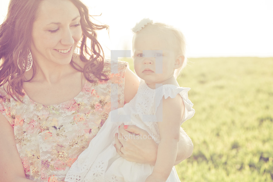 Smiling mother holding daughter in a sunny field.