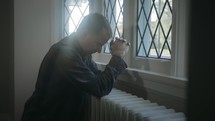man praying at a window 