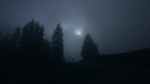 Silhouette of a hiker walking in a dark misty forest at night