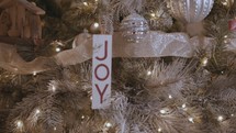 Joy ornament on a Christmas tree with gold ribbon and lights