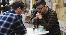 Two men praying on a cafe patio
