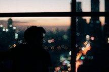 silhouette of a man sitting in a window with the view of a city behind him 