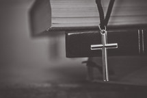 cross necklace hanging from a stack of Bibles 