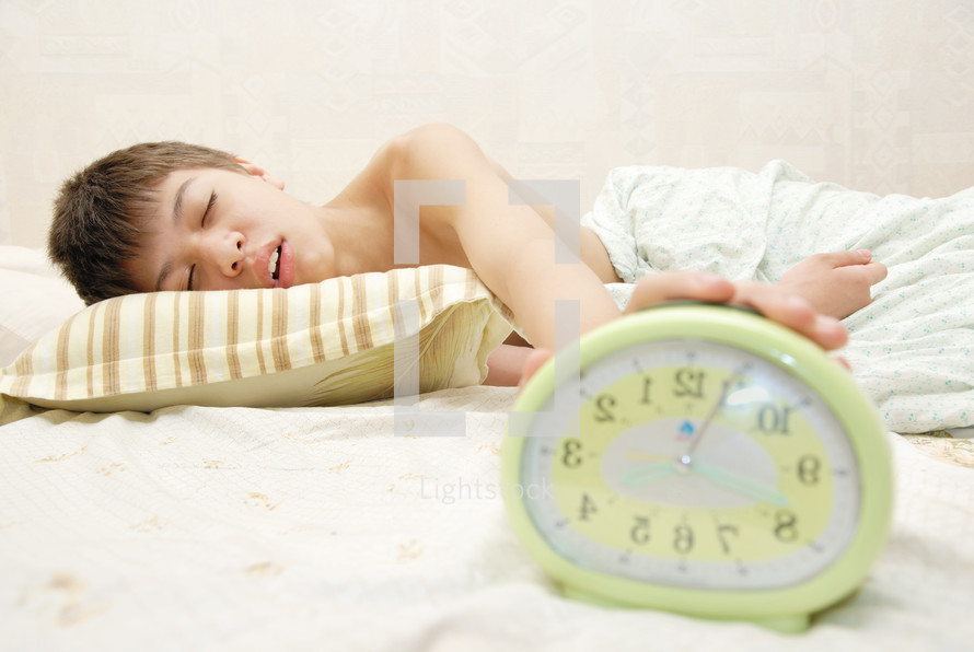 sleepy teen boy hitting an alarm clock 