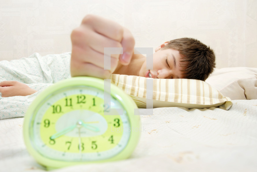 a sleepy teen boy hitting an alarm clock 