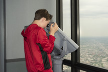 boy looking down at a city through a viewfinder scope 