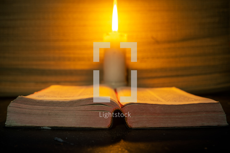 candle light and holy bible on wooden table in the night time.