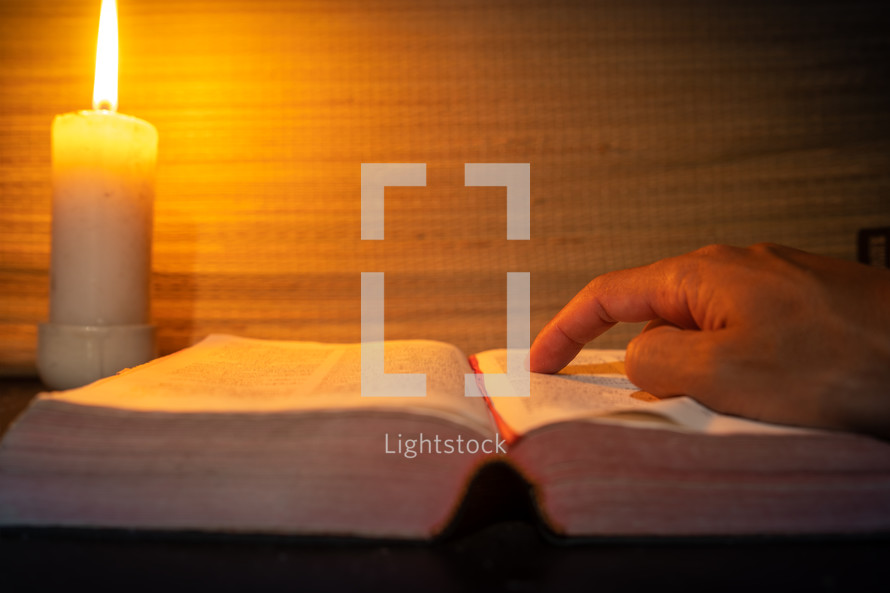 candle light with hands reading bible on wooden table in the night time.