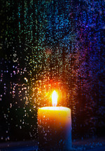 glowing candle behind a wet window 