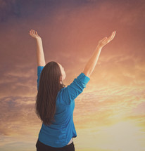 Woman with arms raised under and orange sky.