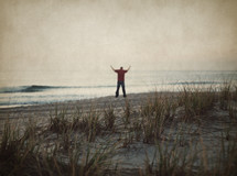 man standing on a beach with his hands raised in praise and worship to the lord