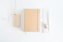 iPhone, journal, earbuds, and pencil on a white desk 