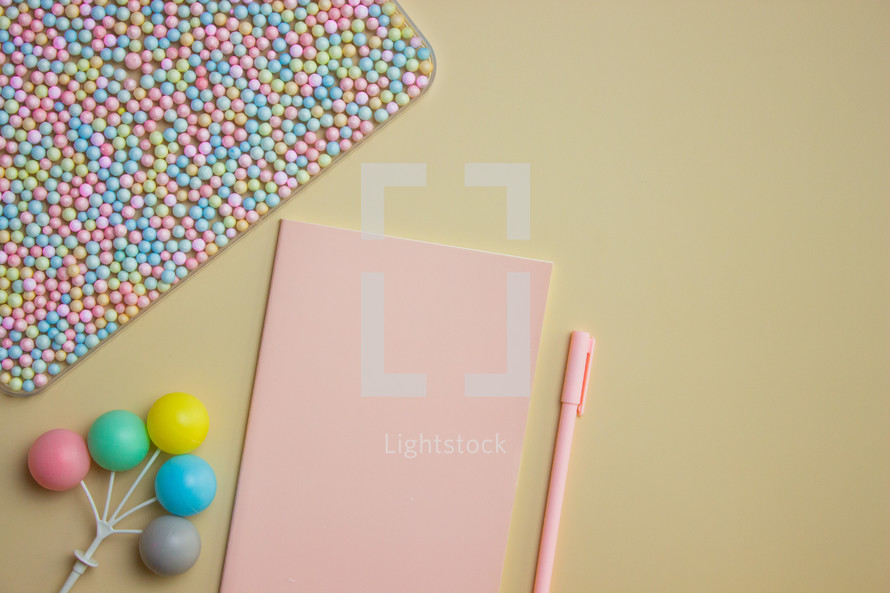 Pink notebook with pen and colorful balls over the brown background. 