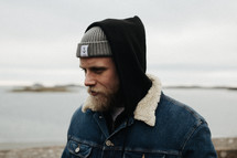 a man in a beanie standing by a shore 