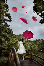 A woman standing on a bridge with umbrella- sky full of umbrellas