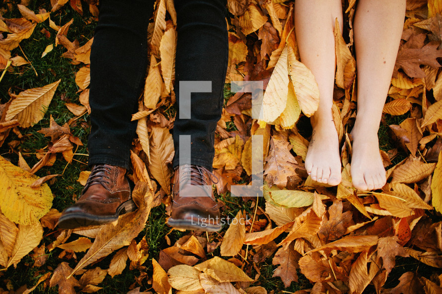 feet of a couple lying in a pile of leaves 