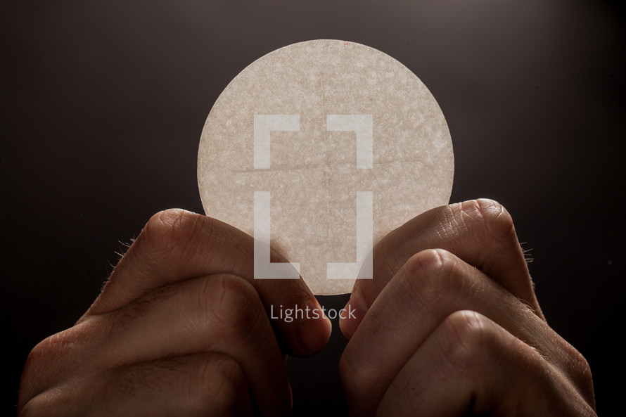 Hands holding a single communion wafer.