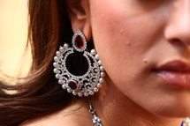 A woman wearing a very large earring with gemstones and pearls.