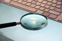 A magnifying glass held over a computer keyboard.